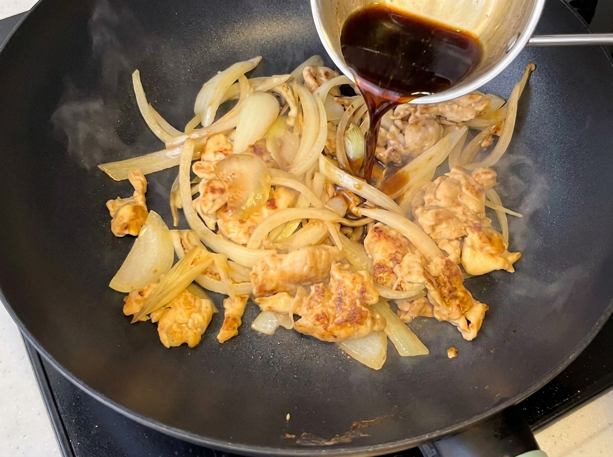 Salsa scura versata in una padella contenente pollo e cipolle ammorbidite.