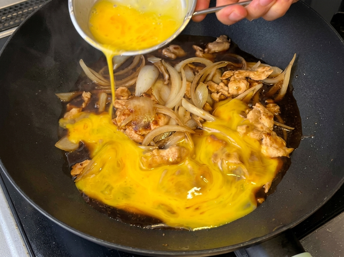 Uova sbattute versate sul composto di pollo, cipolla e salsa in padella.