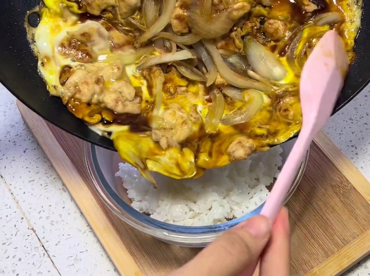 Primo piano del composto di pollo, uova e cipolla trasferito dalla padella a una ciotola di riso bianco fumante.