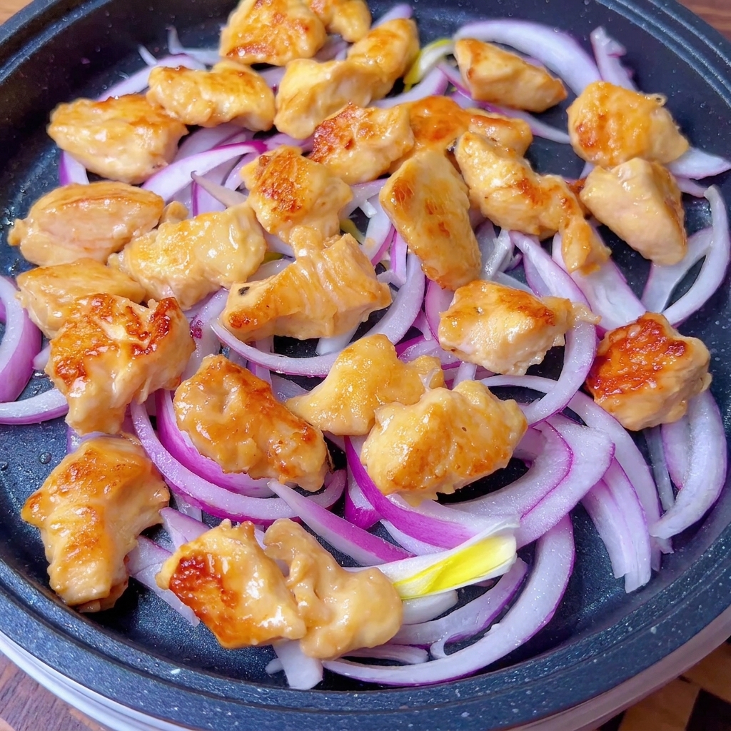 Pollo dorato e cipolle teneri ricoperti dalla salsa in padella.