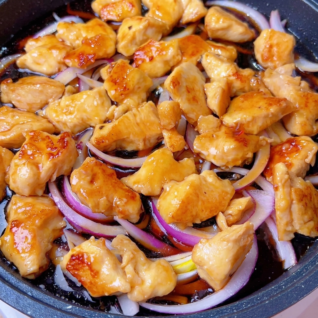 Una padella coperta sul fornello con il composto di pollo e cipolla che sobbolle.