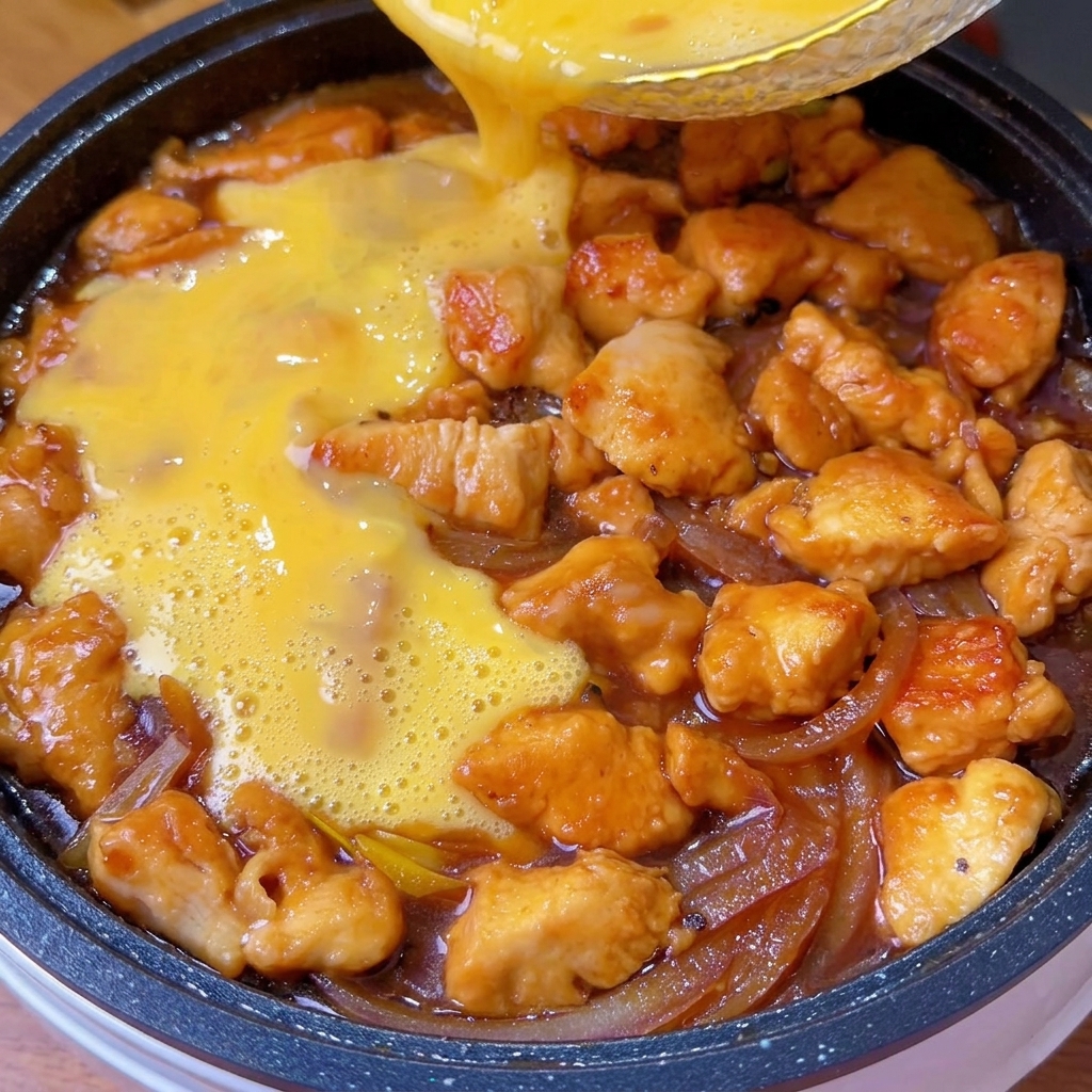Uova sbattute versate sopra il composto di pollo e cipolla in padella.