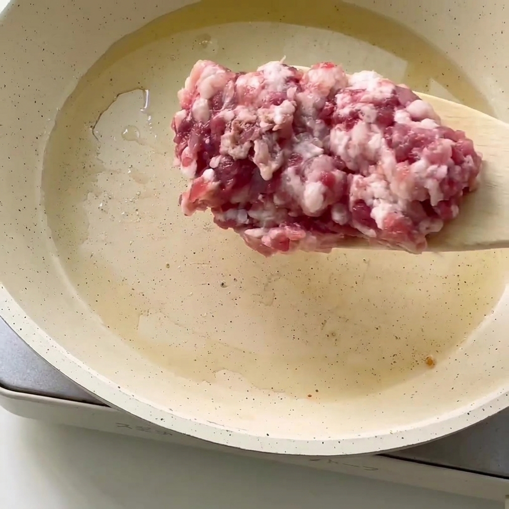 Primo piano della carne macinata fresca aggiunta in una padella con olio caldo.