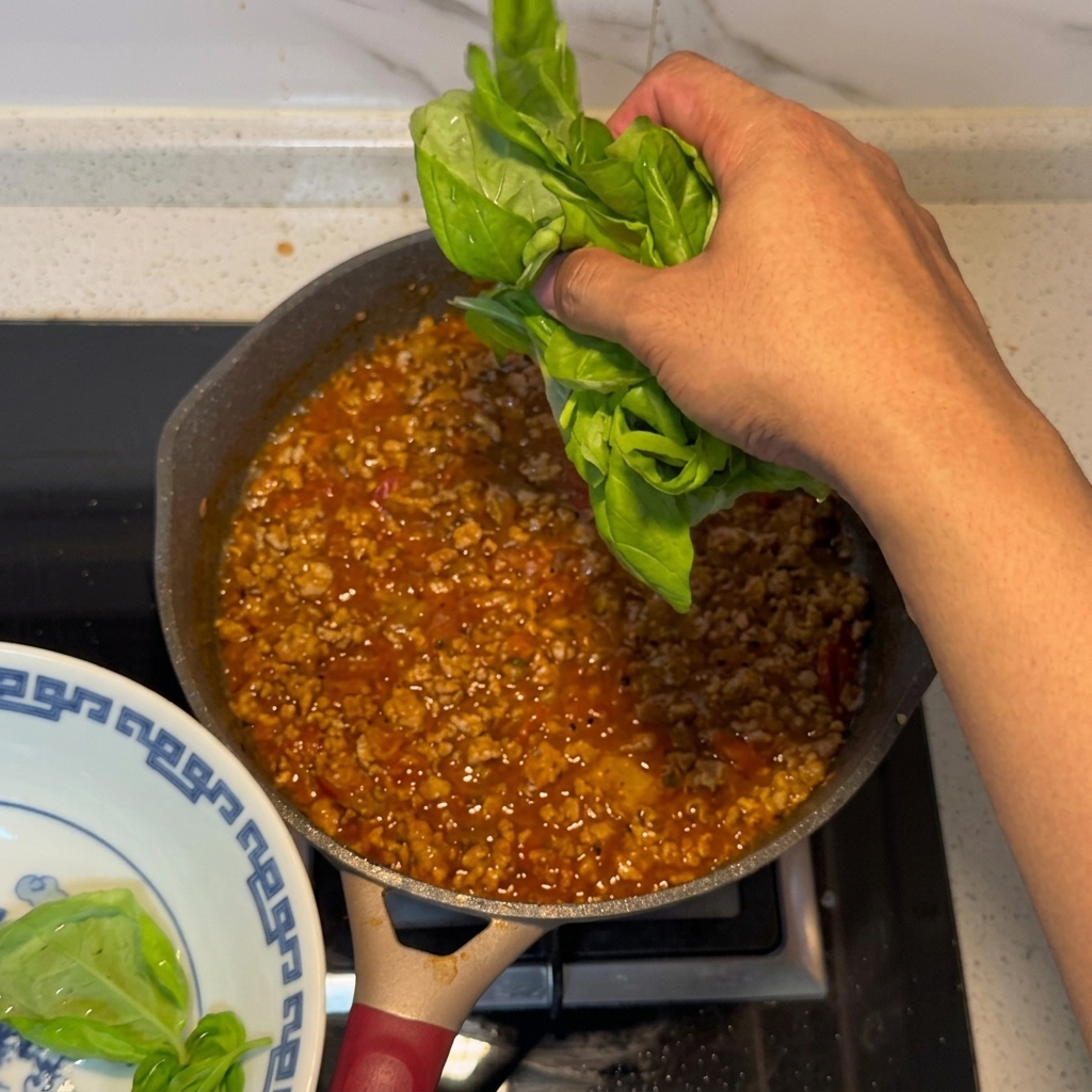 Foglie di basilico fresco aggiunte al sugo di carne e pomodoro pronto.