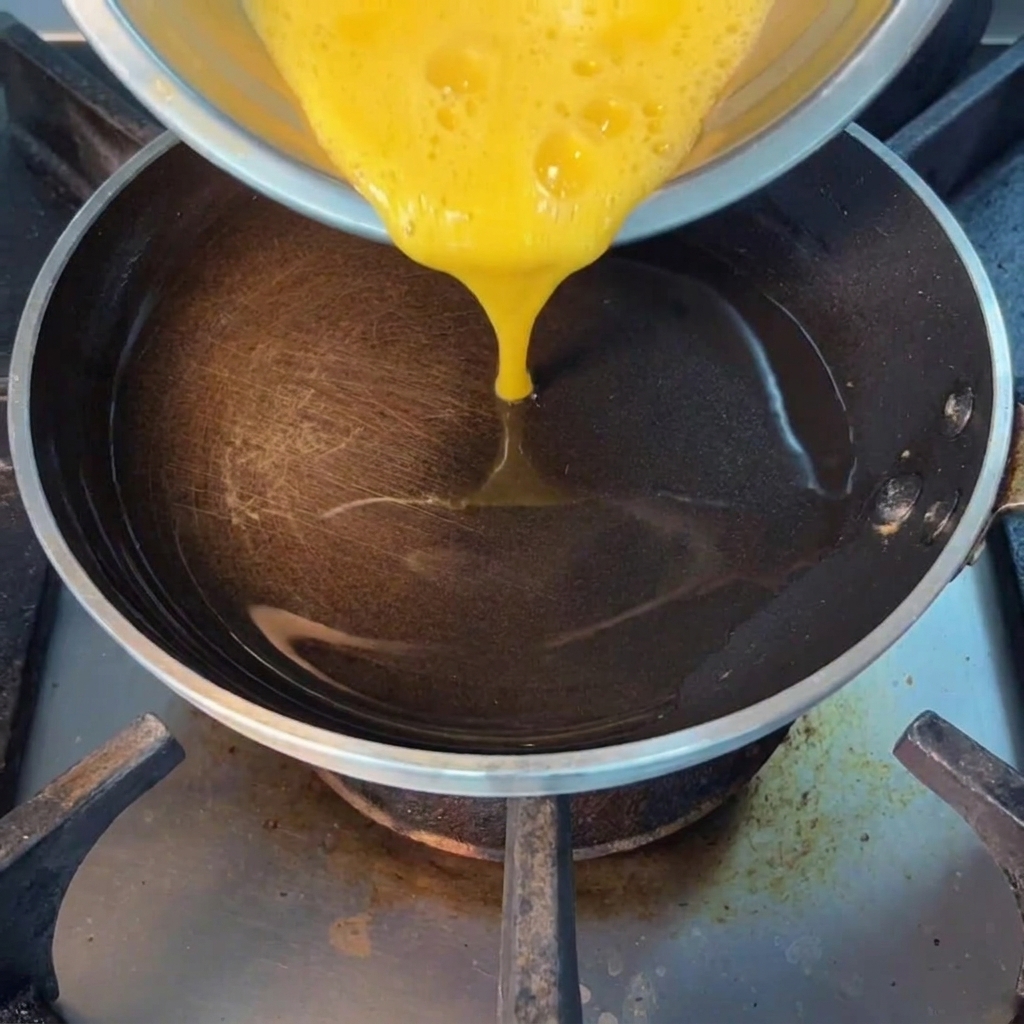Primo piano di uova sbattute versate in una padella calda oliata.