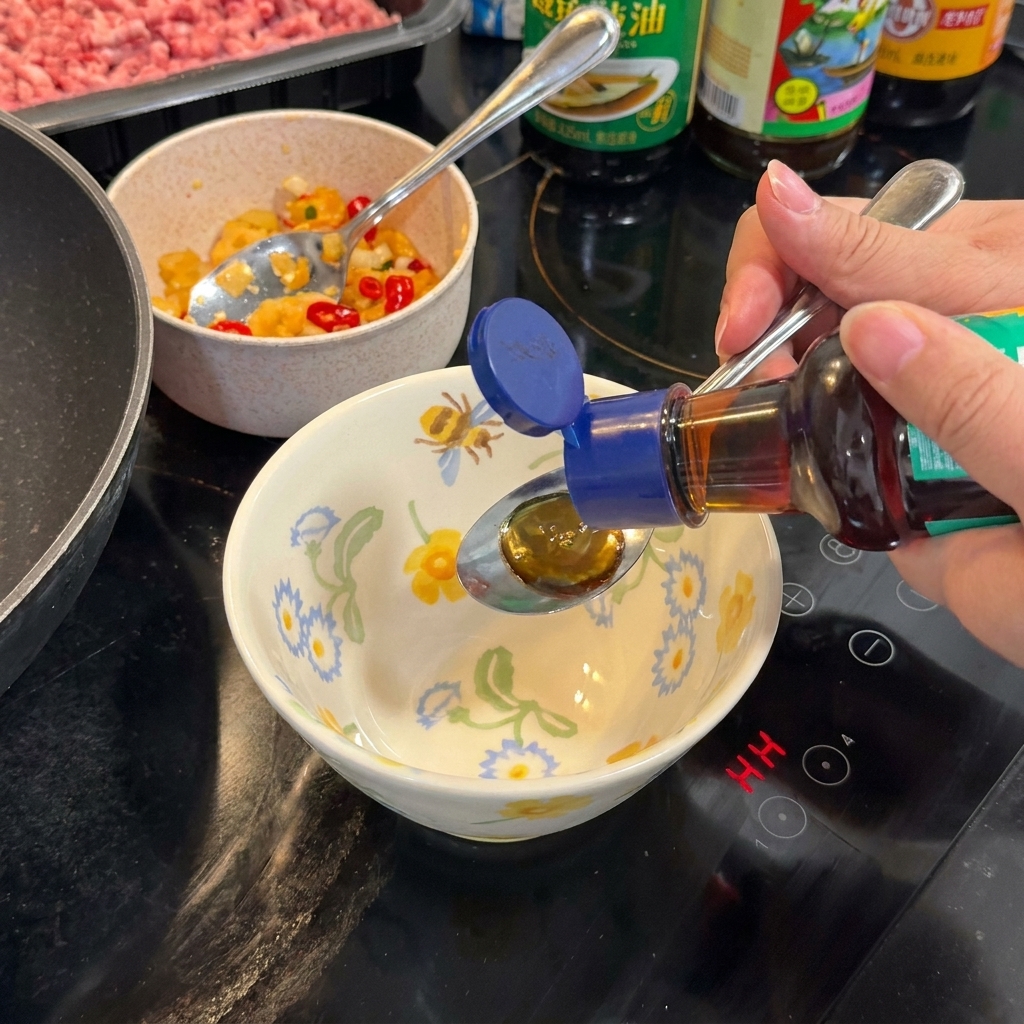 Un cucchiaio che mescola una salsa scura e saporita in una ciotola a motivi floreali sul fornello.