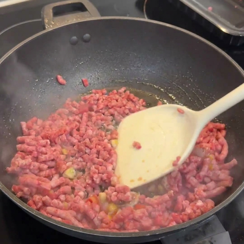 Macinato di manzo Wagyu che rosola in un wok con aglio e peperoncini, separato con una spatola bianca.