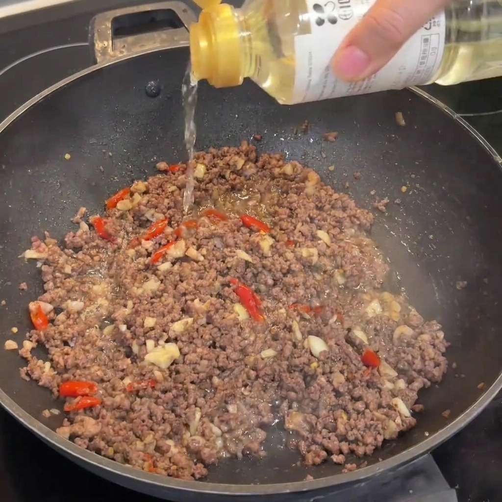 Un goccio di vino di riso versato in un wok contenente macinato di manzo rosolato.