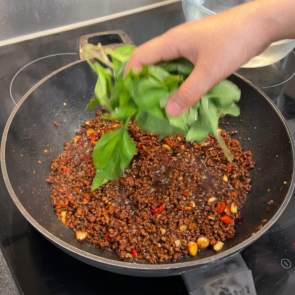 Unampia manciata di foglie di basilico sacro fresco aggiunte a un wok con manzo condito, pronte per essere appassite.