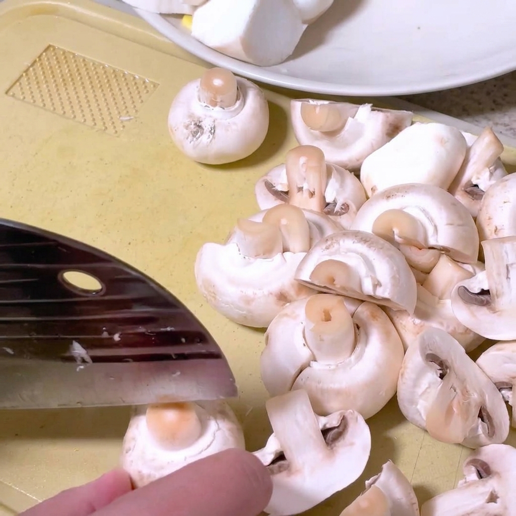 Funghi champignon tagliati a metà su un tagliere con un coltello da cucina.