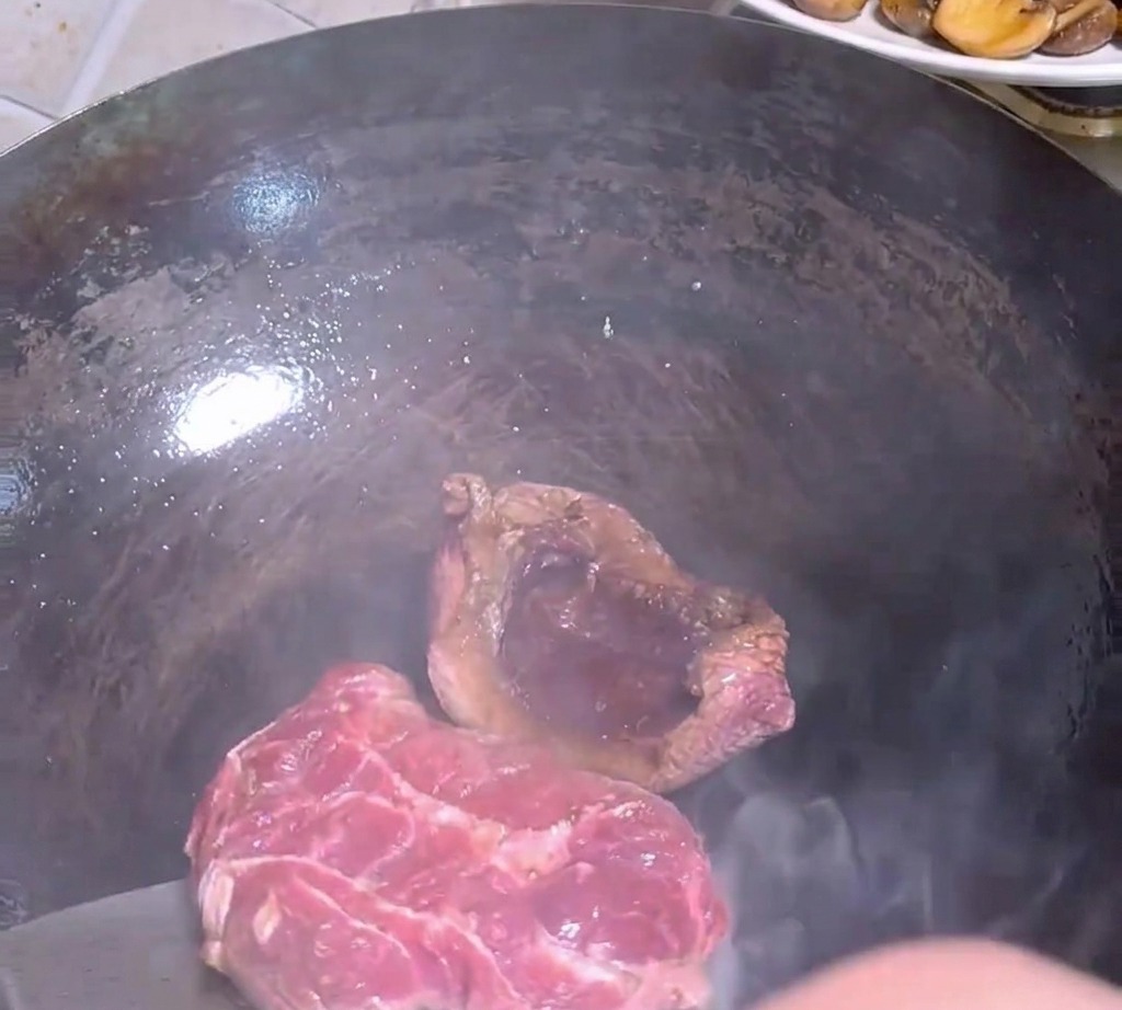 Una spatola di metallo gira un pezzo di manzo nel wok bollente.