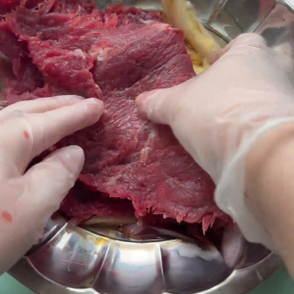 Una fetta di manzo mescolata nella marinata di uovo, cipolla e salse in una ciotola.