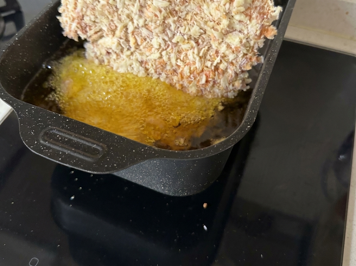 Una cotoletta di manzo impanata che frigge in una padella con olio bollente.