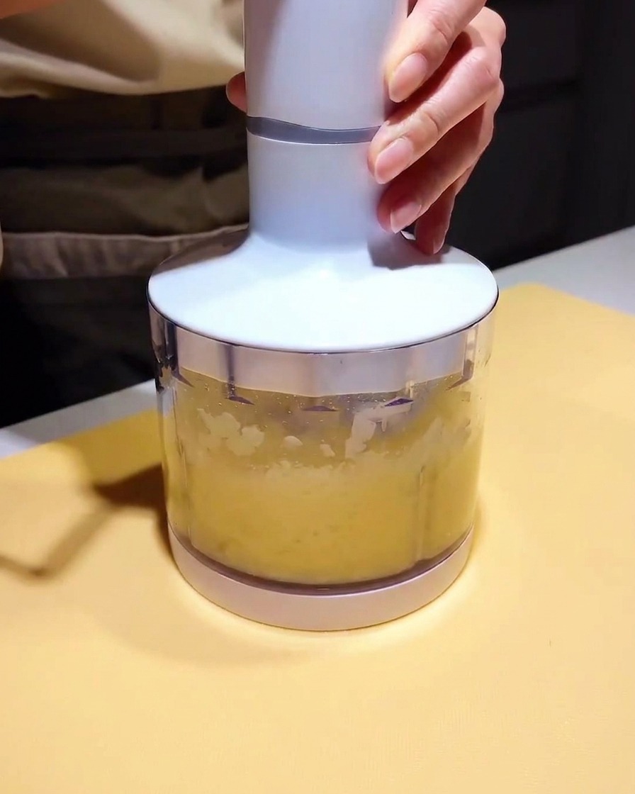 Un piccolo bicchiere da frullatore riempito con una purea chiara e una base di marinatura scura, pronto per essere frullato.