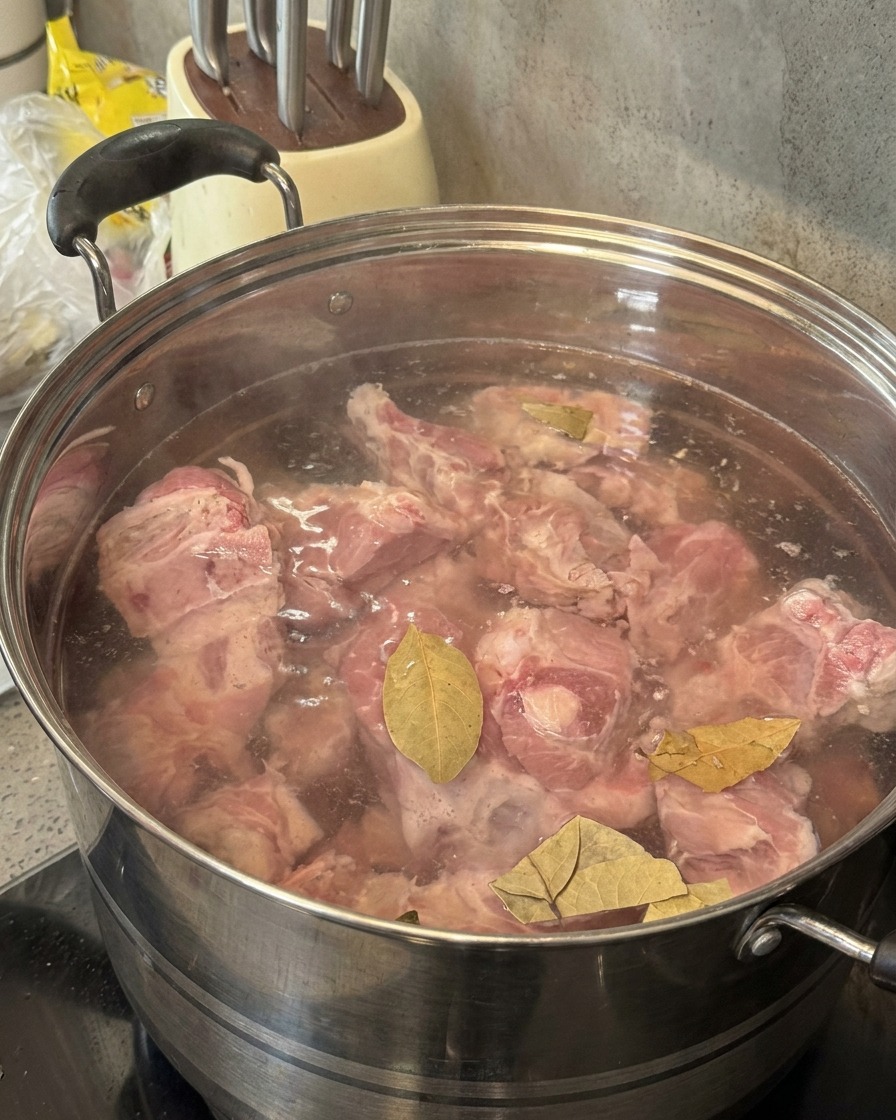 Soju versato da una bottiglia verde in una pentola contenente ossa di maiale e foglie di alloro.