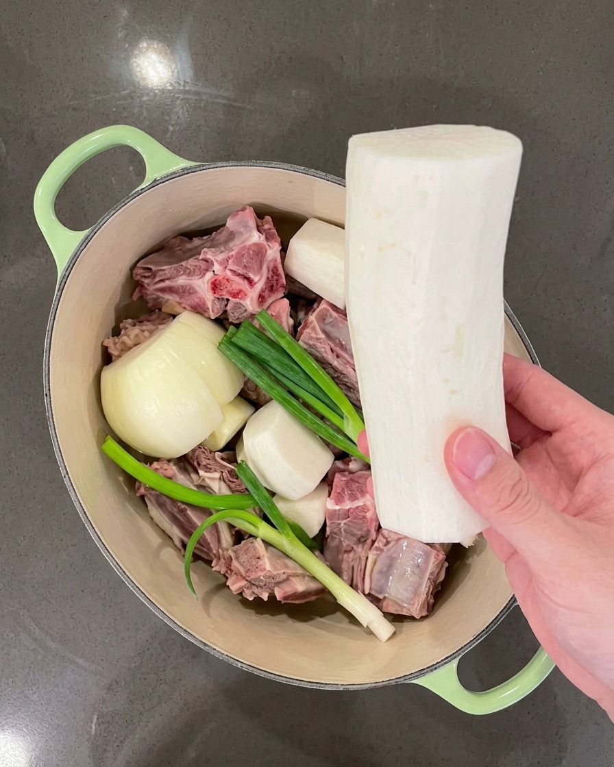 Mano che mette grandi pezzi di ravanello bianco nella pentola insieme alla carne e agli aromi.