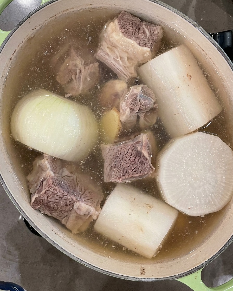 Un mestolo nero che schiuma via la schiuma galleggiante dalla superficie del brodo che bolle.