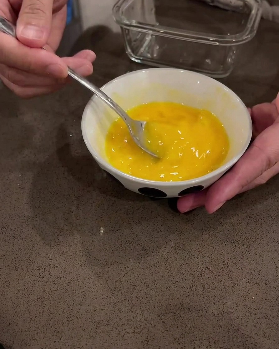 Uova crude sbattute in una ciotola bianca con un cucchiaio di metallo.