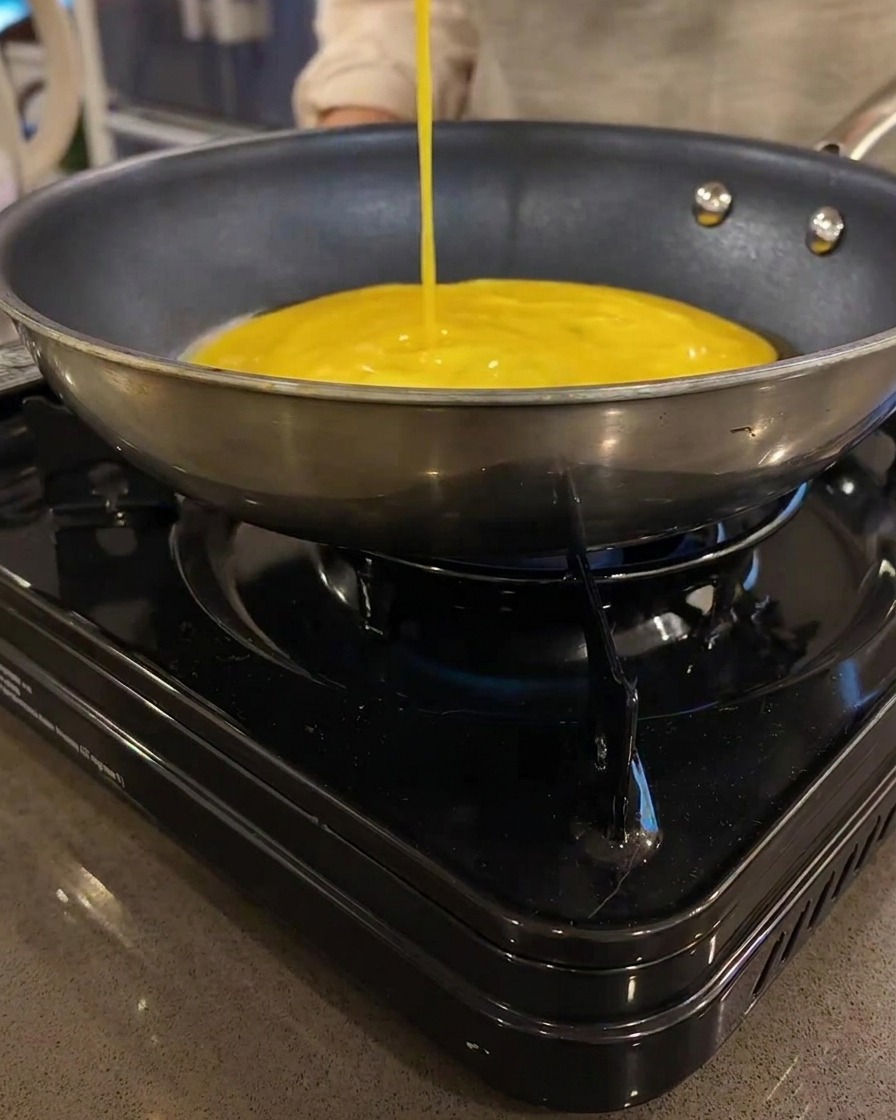 Una sottile crêpe di uova gialla che cuoce in una padella piatta su un fornello portatile.