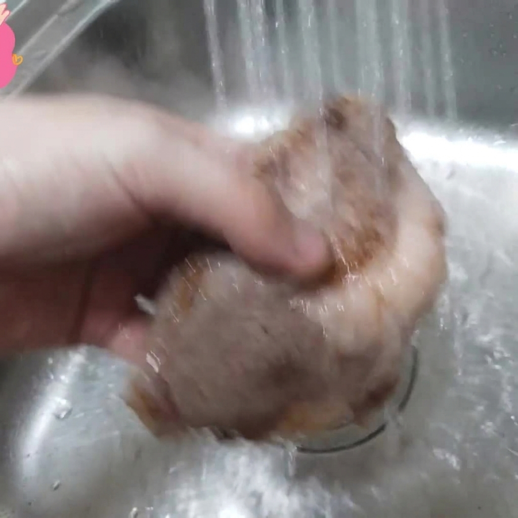 Un pezzo di costina di manzo sbollentata tenuta sotto lacqua corrente in un lavandino.
