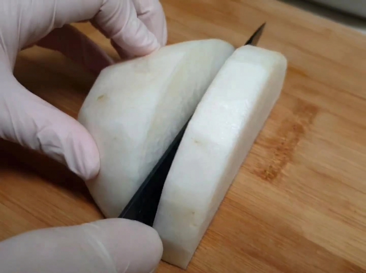 Ravanello bianco affettato su un tagliere di legno, mani che indossano guanti per alimenti.
