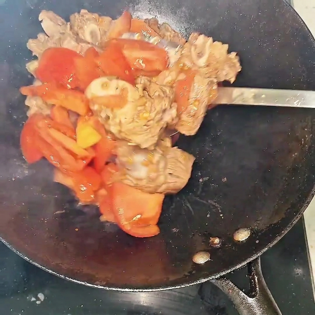Primo piano di costine e pomodori che soffriggono nel wok formando liquido.