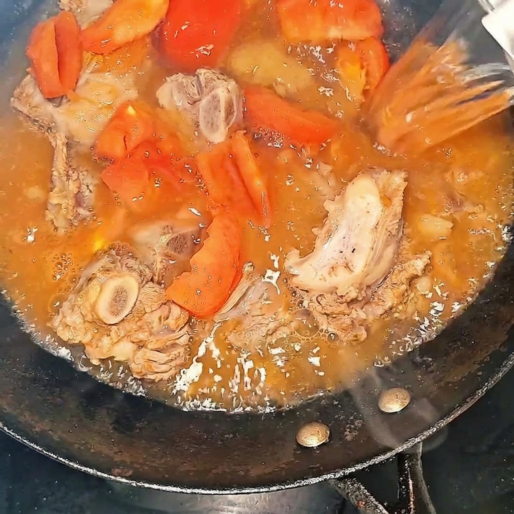 Acqua bollente versata nel wok con costine e pomodori.