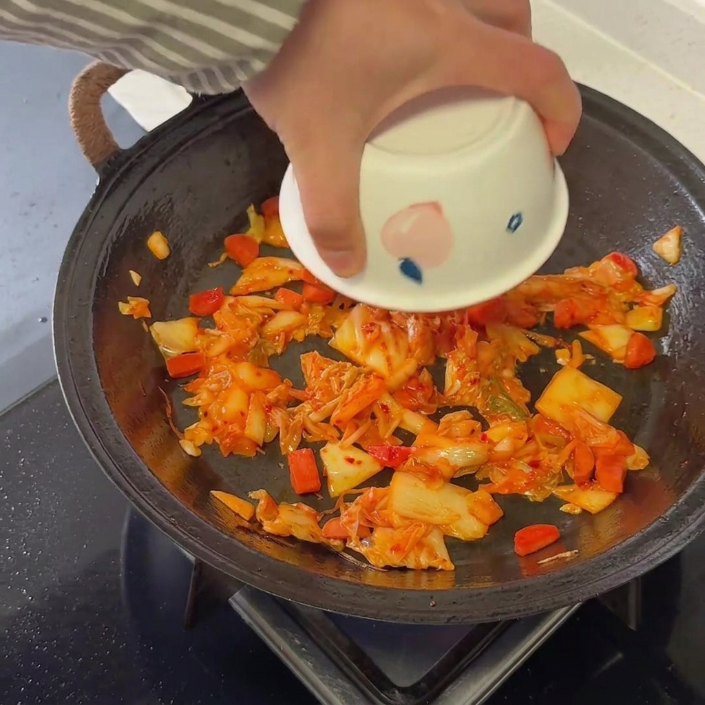 Riso cotto aggiunto alla base di kimchi e salsiccia in una padella calda.
