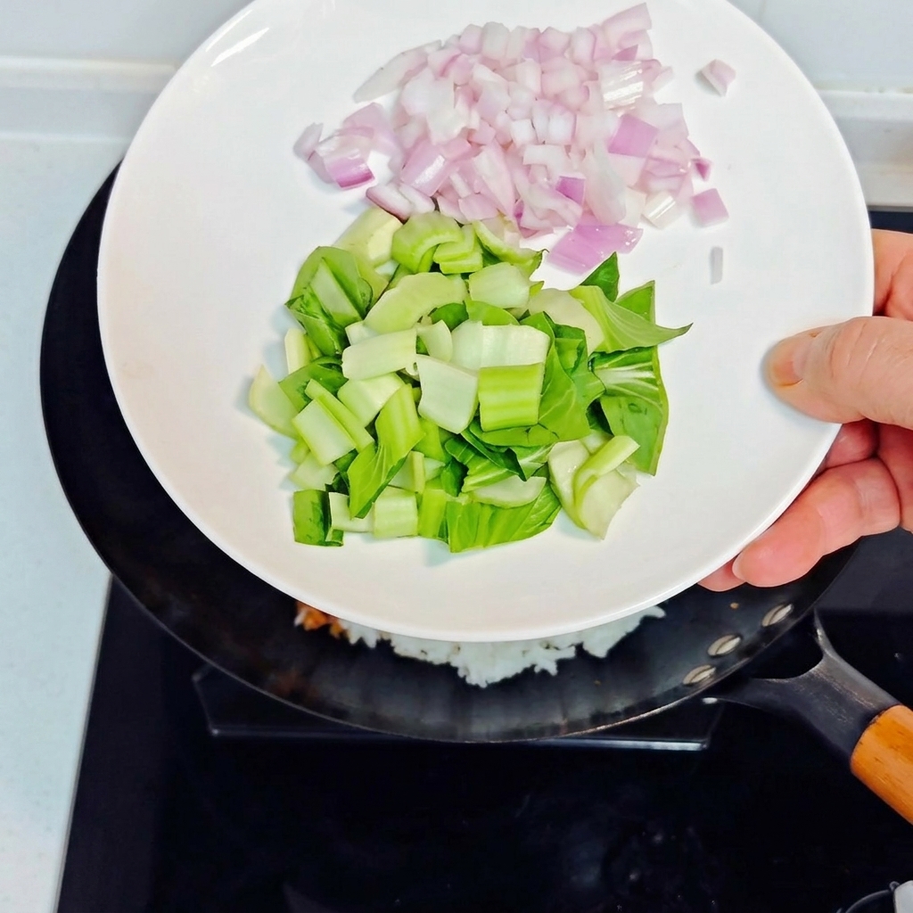 Versare cipolle viola a cubetti e bok choy tritato da un piatto bianco nel wok con il riso fritto.