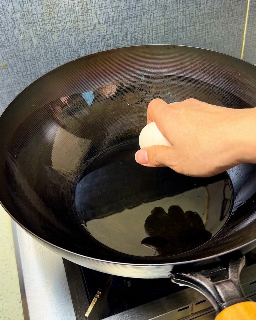 Due uova crude lasciate cadere in un wok caldo e condito pieno di olio sfrigolante.