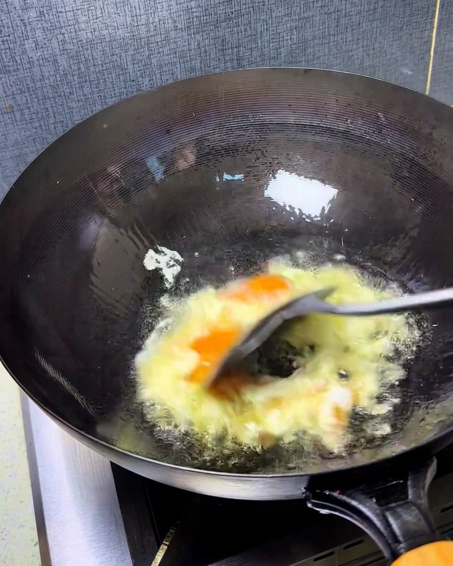 Uova sbattute rapidamente in un wok caldo con una spatola, creando pezzi soffici e dorati.