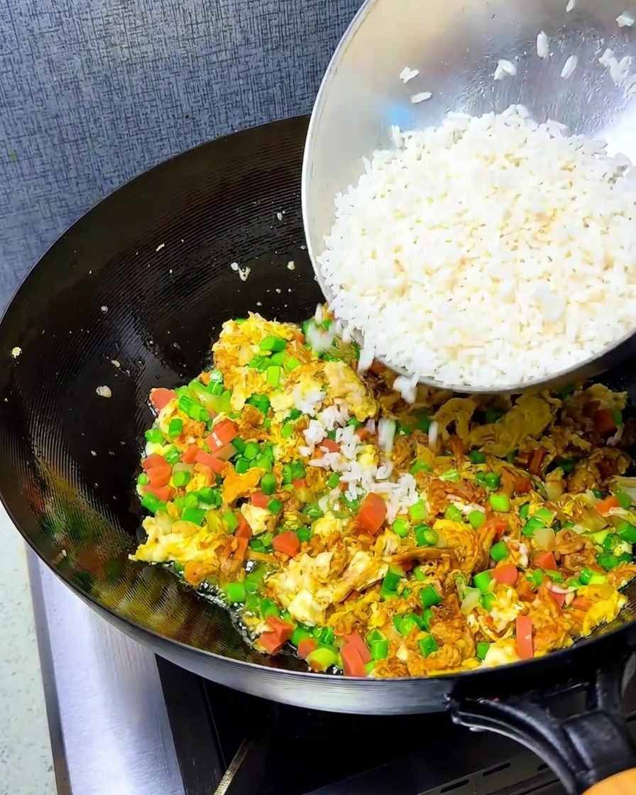 Riso bianco sgranato aggiunto al wok contenente le uova saltate in padella e il mix di verdure.