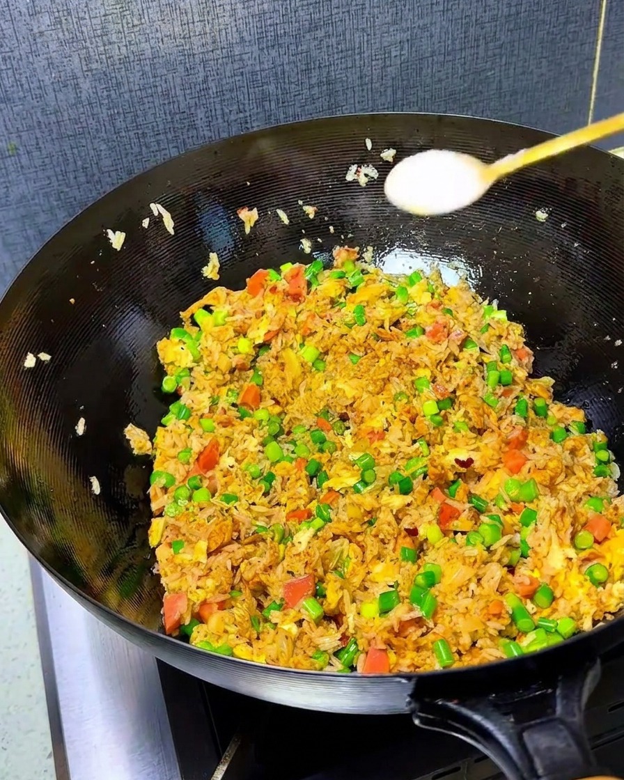 Primo piano di sale e brodo di pollo in polvere cosparsi in un wok pieno di colorato riso fritto al kimchi.