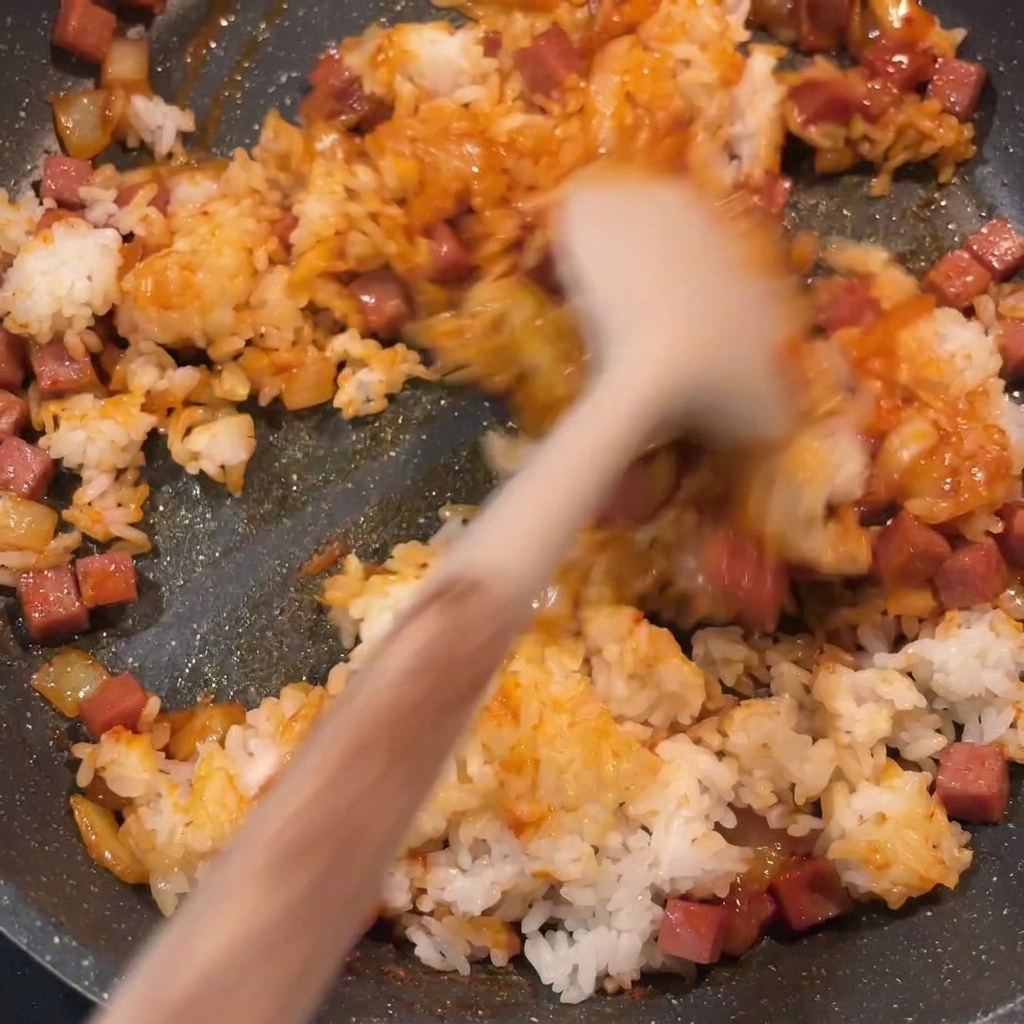 Il riso saltato al kimchi pronto mentre viene mescolato in padella, mostrando un colore rosso uniforme e pezzi ben distribuiti.