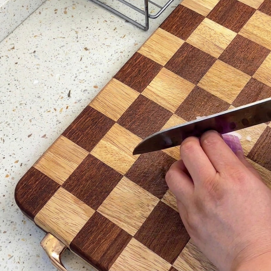 Primo piano di scalogni tritati finemente su un tagliere di legno a scacchi con un coltello affilato.