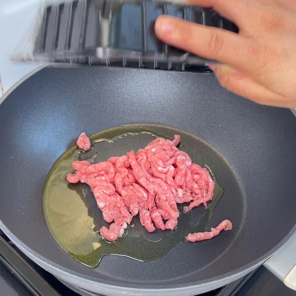 Maiale macinato aggiunto in una padella con olio caldo e saltato con una spatola di legno.