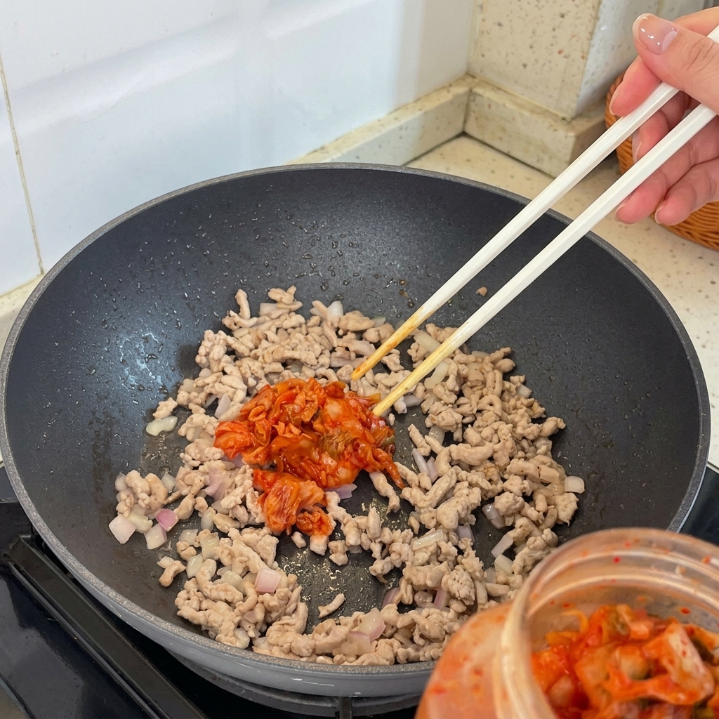Pezzi di kimchi aggiunti al composto di carne e scalogni che salta nella padella.