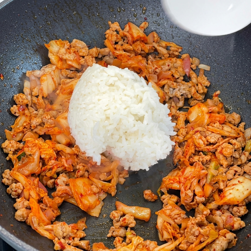 Riso bianco cotto aggiunto a una padella piena di maiale macinato e kimchi saltati.