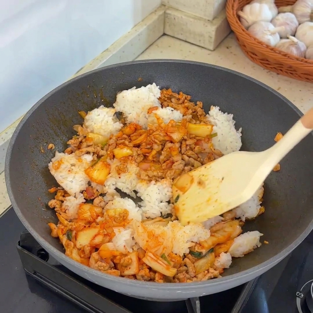 Una spatola che mescola vigorosamente il riso, la carne e il kimchi in un wok caldo.