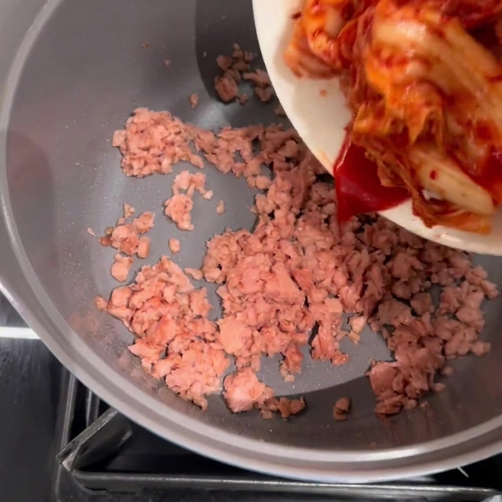 Il kimchi viene aggiunto nella pentola con lo Spam rosolato.