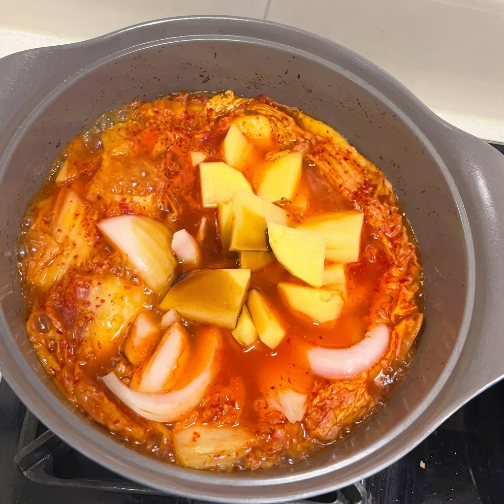 Pezzi di cipolla e patata aggiunti allo stufato di Spam e kimchi in ebollizione.