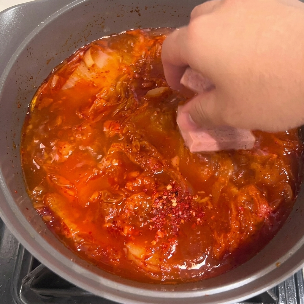 Fette di tofu adagiate con cura nello stufato di kimchi rosso bollente.