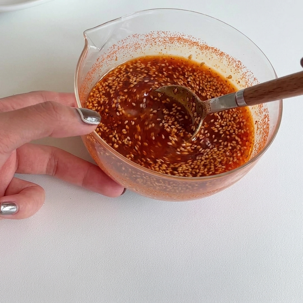 Una mano mescola con un cucchiaio di legno una salsa rossa liscia e vibrante in una ciotola di vetro fino a renderla perfettamente omogenea.