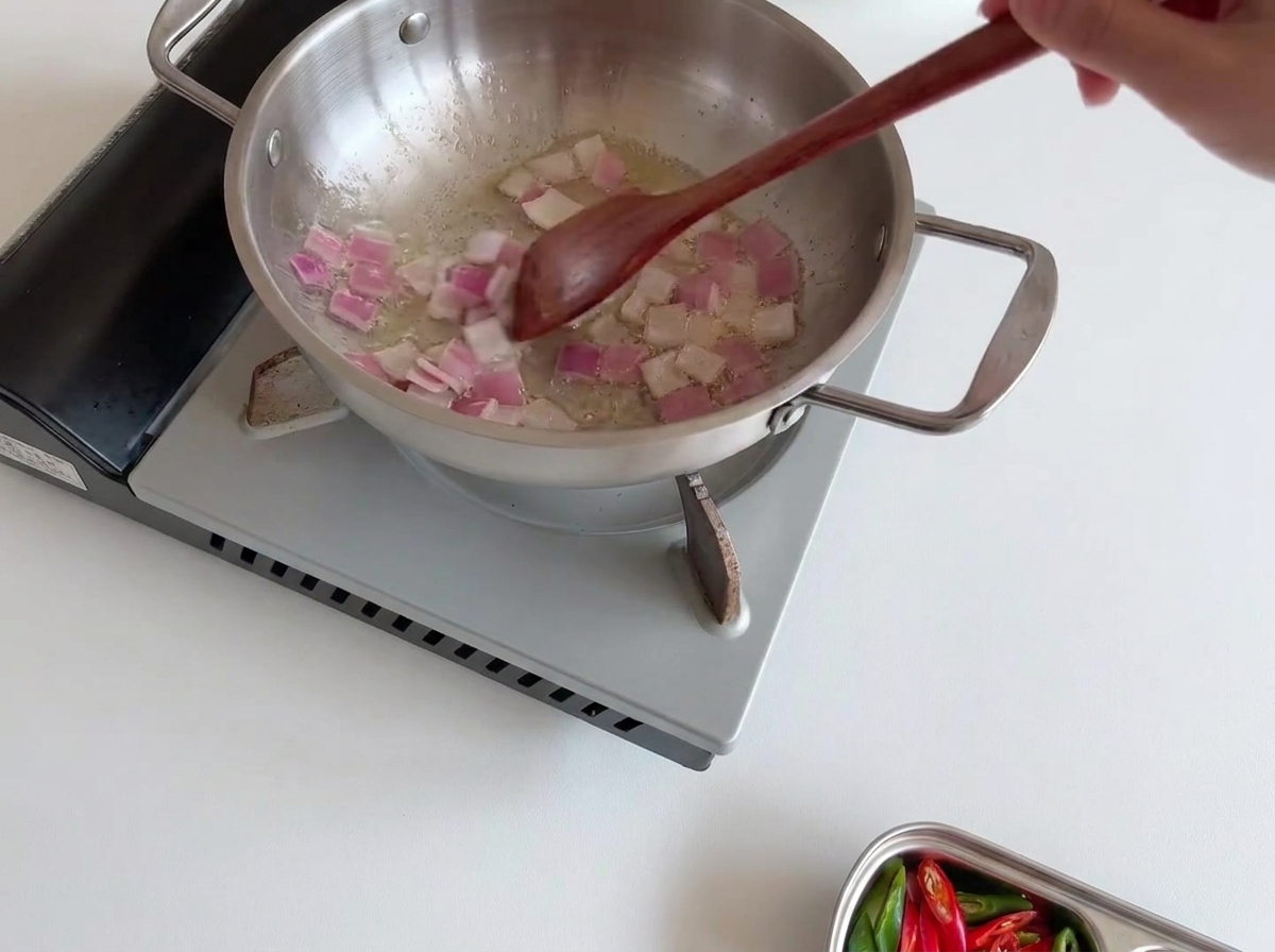 Uno strato fresco e uniforme di funghi enoki bianchi posizionato con cura sopra le cipolle saltate nella padella di acciaio inossidabile.