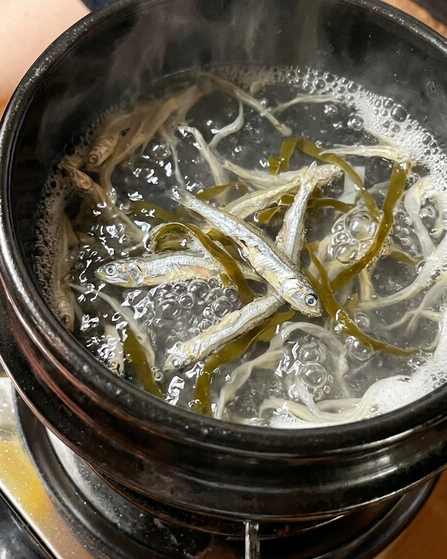 Piccoli pesciolini dargento e pezzi di alga che bollono in una pentola dacqua.