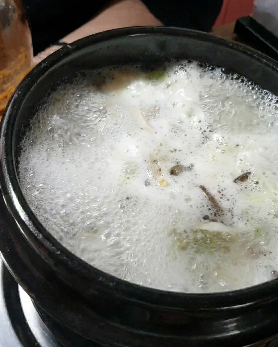 Una grande cucchiaiata di densa pasta di soia scura che viene mescolata nel brodo in ebollizione.