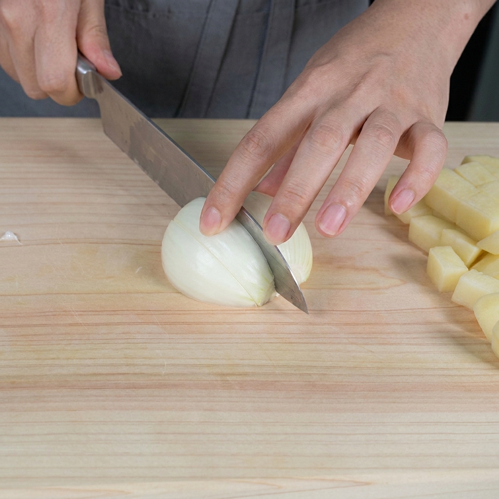 Mani che tritano una cipolla bianca cruda in piccoli pezzi su un tagliere di legno chiaro.