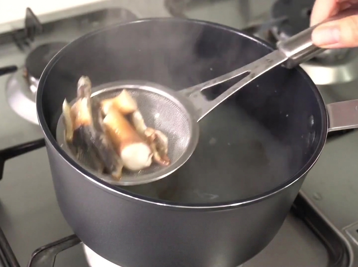 Un colino di metallo che solleva acciughe e alghe ammorbidite dal brodo caldo e limpido.