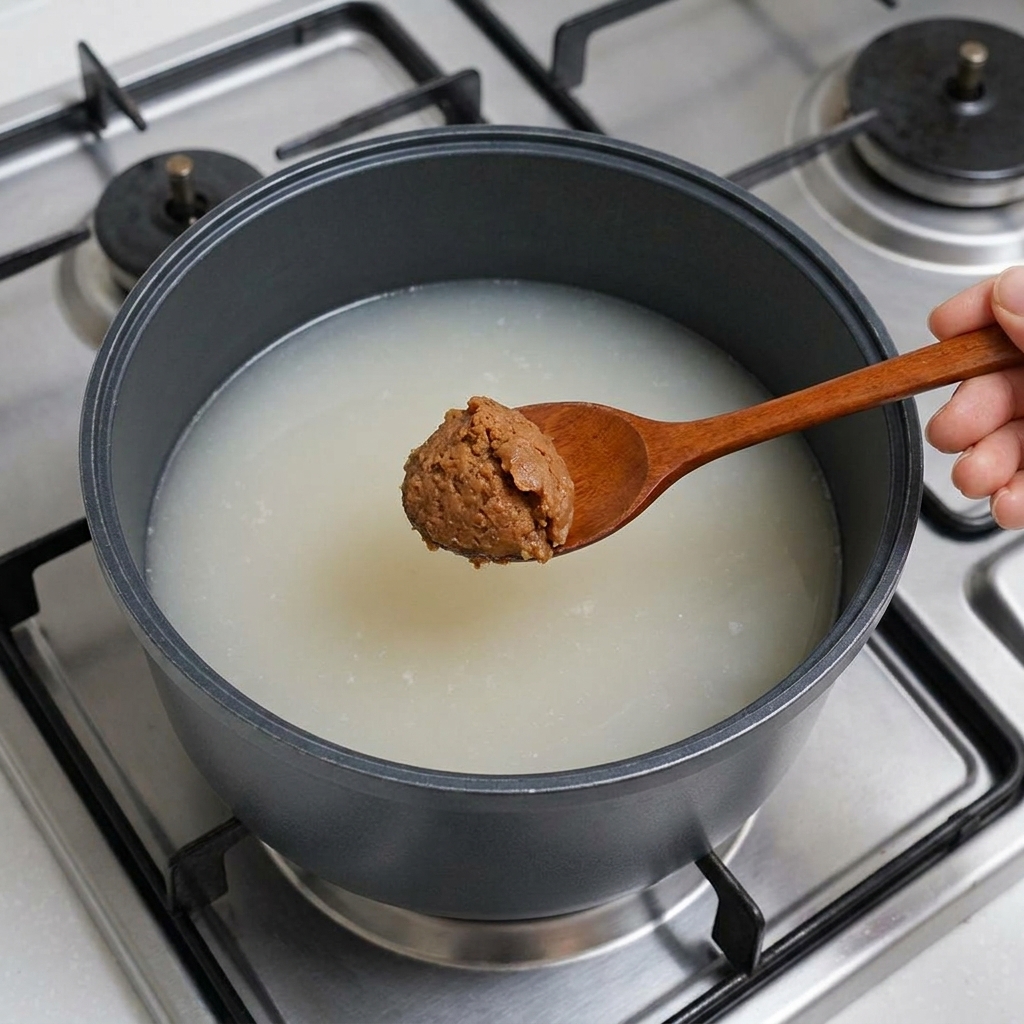 Un cucchiaio di legno che tiene una generosa quantità di pasta di soia marrone calata nel brodo.