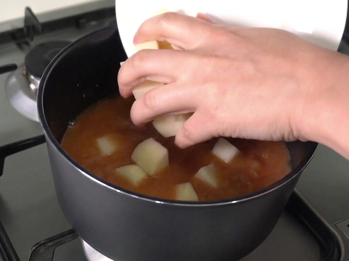 Patate e cipolle tritate fatte scivolare da un piatto bianco in una pentola di brodo rosso bollente.